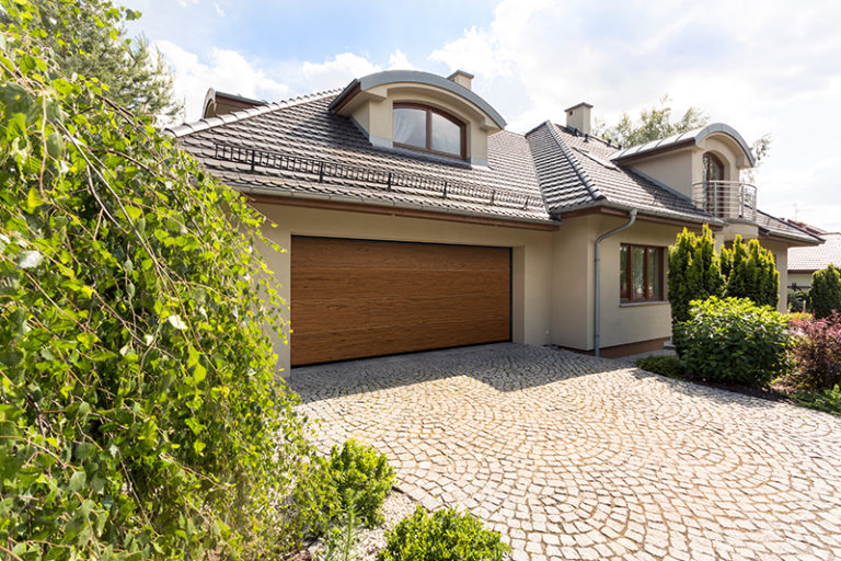 Detached family house exterior with cobblestone driveway to the garage and spruce garden